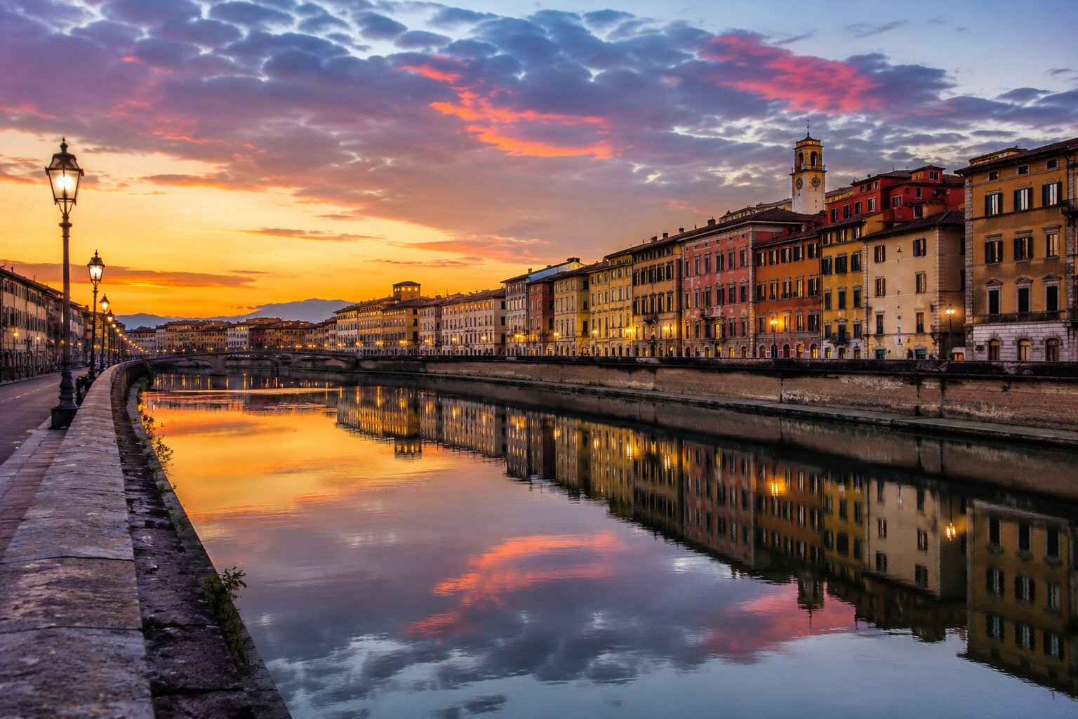 Arno River in Pisa with historic buildings and sunset reflections